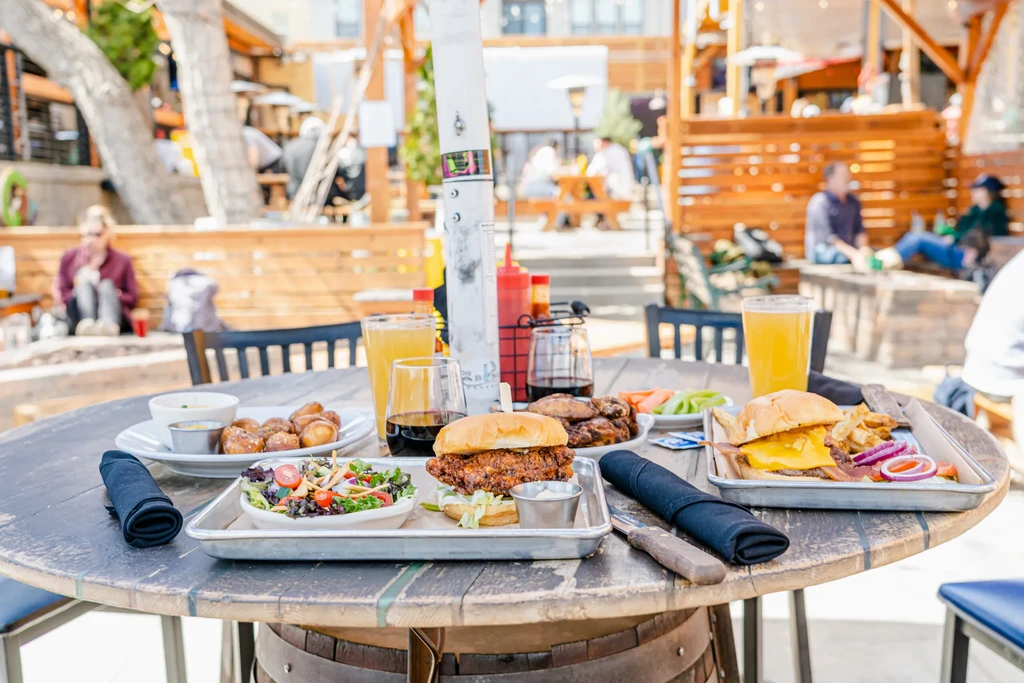 Outdoor patio table laden with burgers, chicken, pretzels, and drinks.