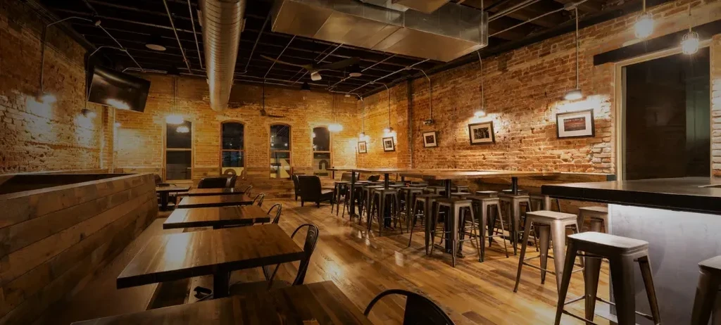 Empty industrial-chic restaurant interior with exposed brick walls and hardwood floor.