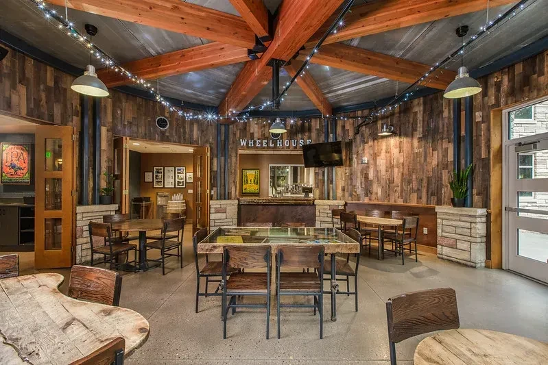 Rustic-industrial restaurant interior with exposed beams, string lights, and wooden tables.