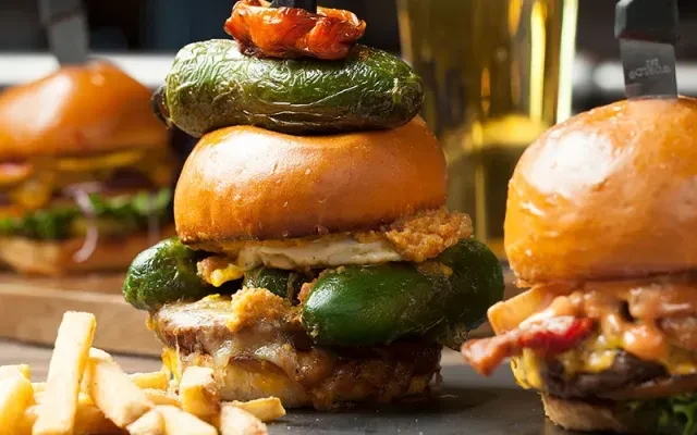 Close-up: multiple gourmet burgers, prominent jalapeños, and french fries.