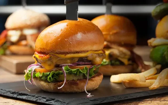 A large, layered burger with fries on a dark board.