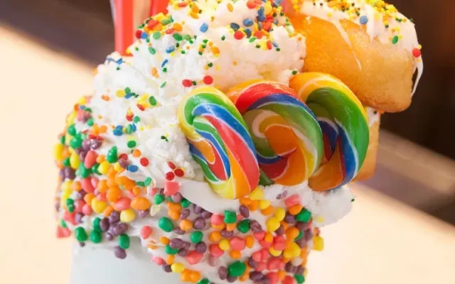 Vibrant freakshake with whipped cream, sprinkles, rainbow lollipops, and a donut.