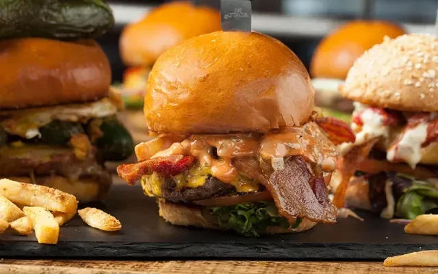 Multiple gourmet burgers and fries on a dark slate board.