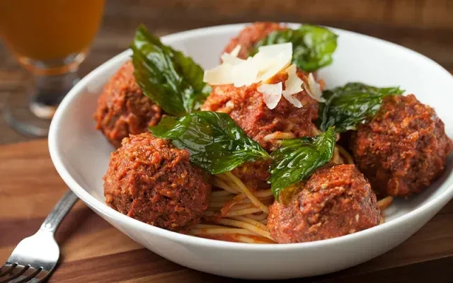 Close-up bowl of spaghetti and meatballs with basil and Parmesan.
