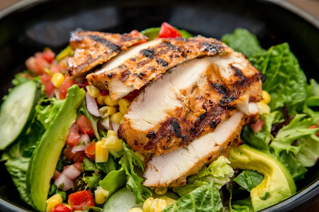 Close-up of grilled chicken salad with avocado and colorful vegetables.