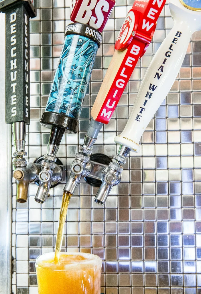 Four beer taps, one actively pouring golden beer into a glass.