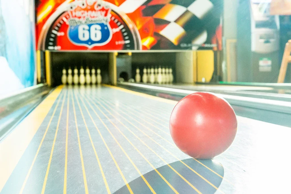Red bowling ball on mini lane, pins, and 'Highway 66' wall sign.