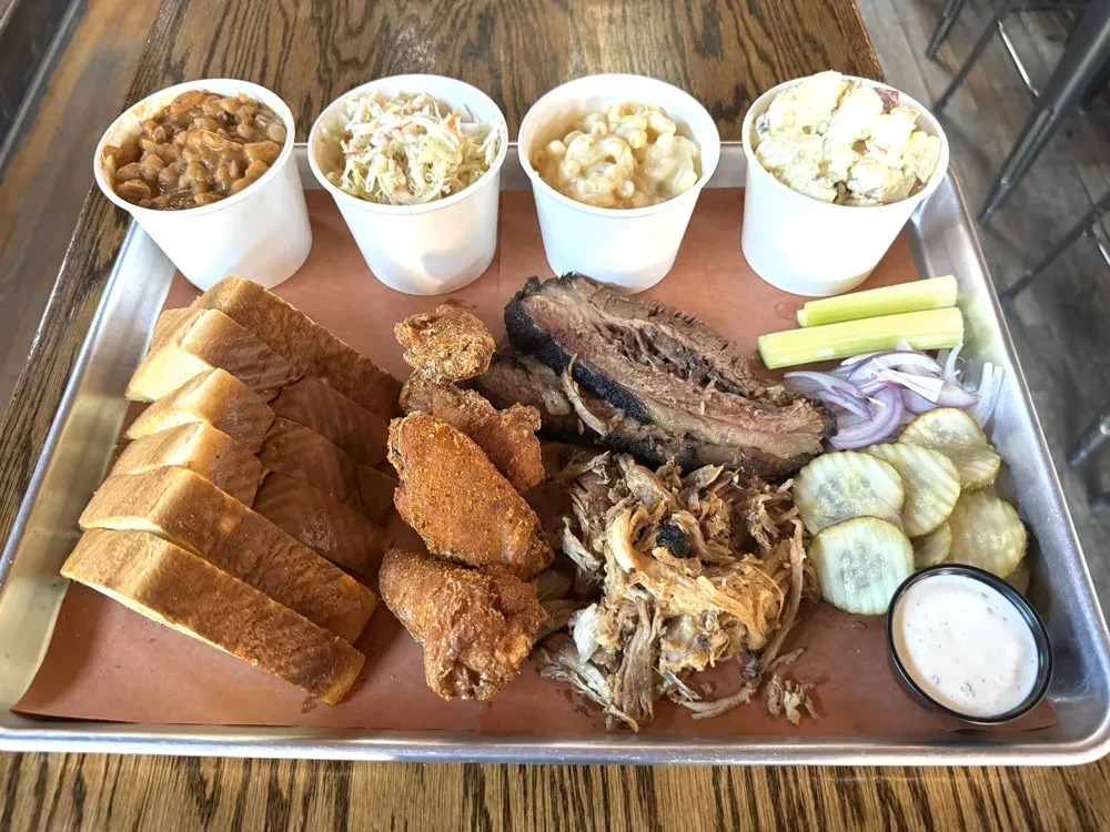Platter with barbecue brisket, pulled pork, chicken wings, and multiple sides.