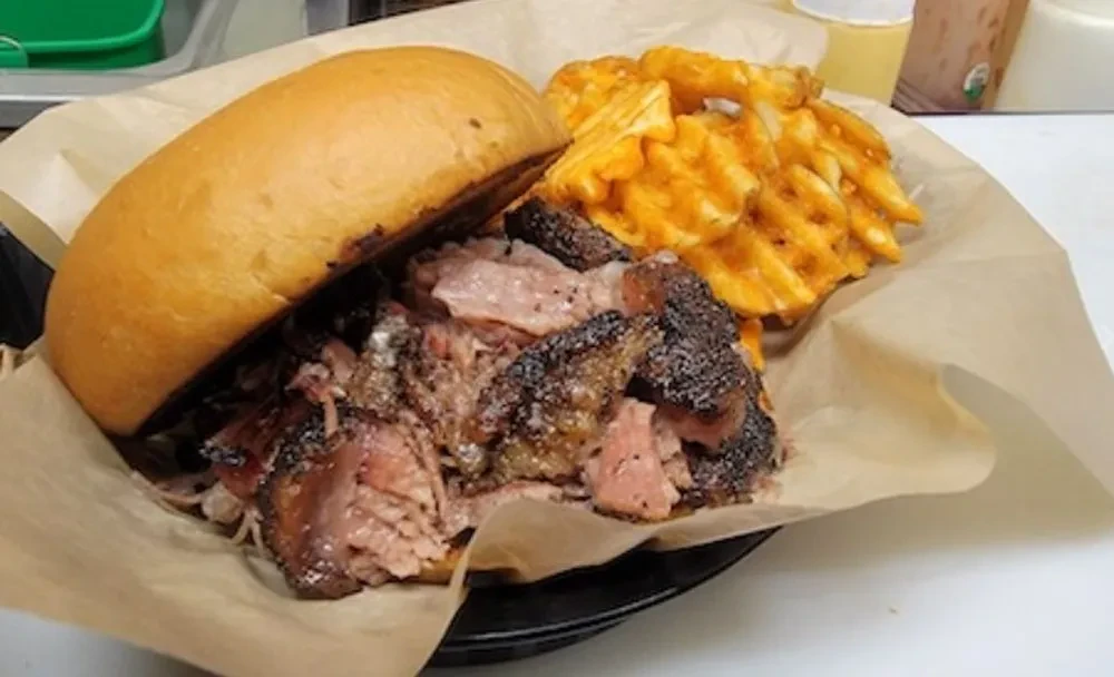 Close-up: Brisket sandwich and golden waffle fries in a bowl.