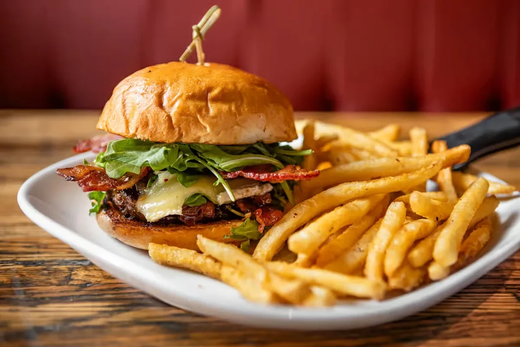 Plate with gourmet burger, melted cheese, bacon, arugula, fries.