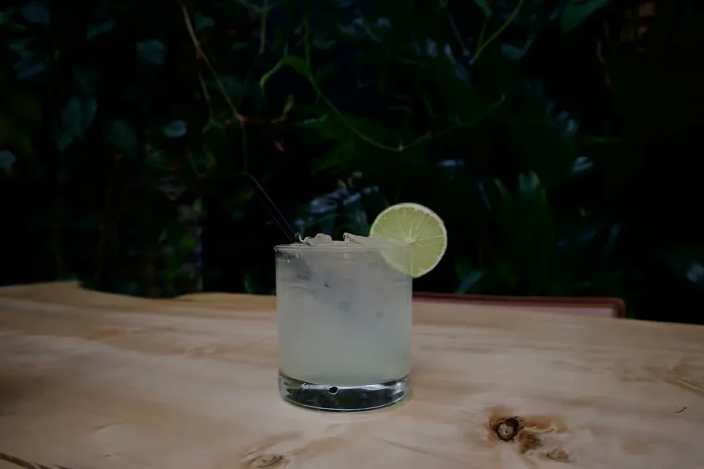 Glass of frosty drink with ice, lime, and straw on wood.
