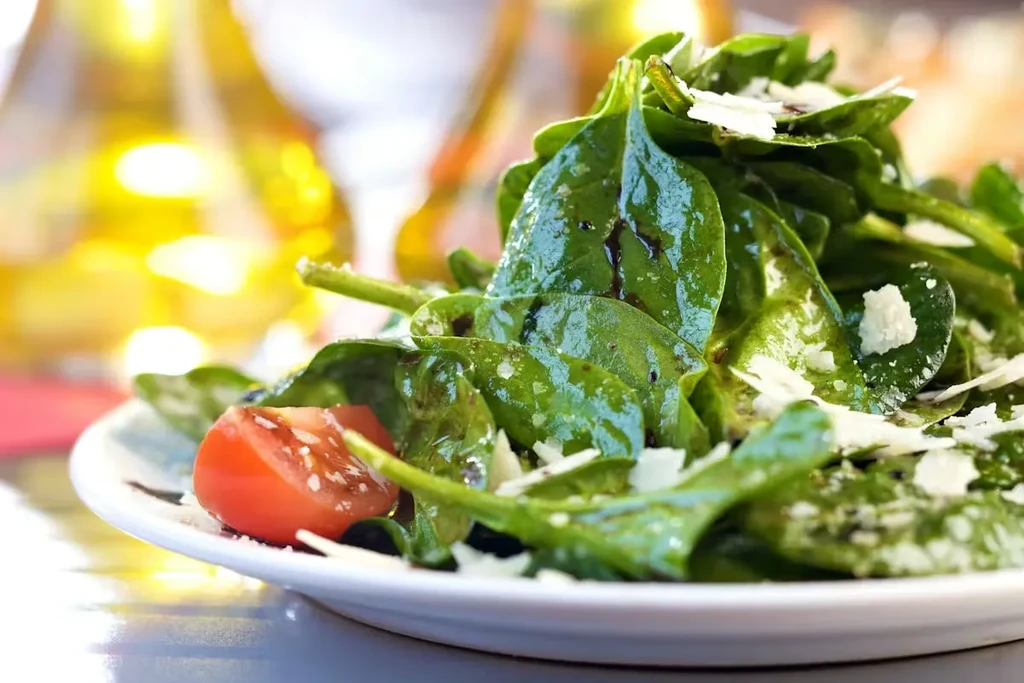 Fresh spinach salad with Parmesan and cherry tomato on a white plate.