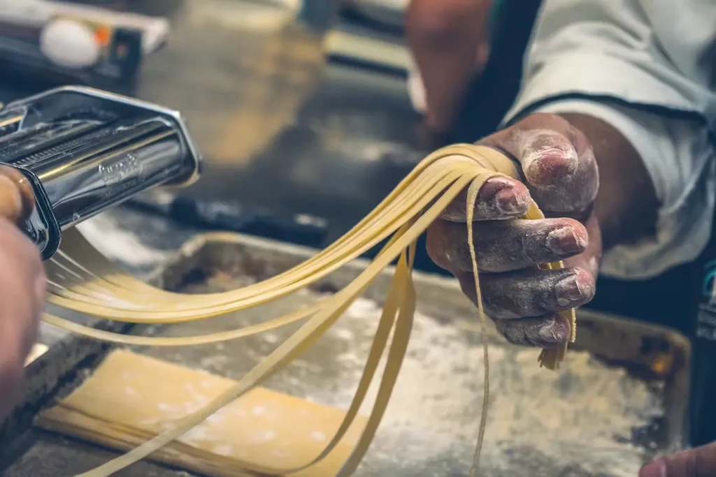 Chef's flour-dusted hands making fresh pasta with a machine.