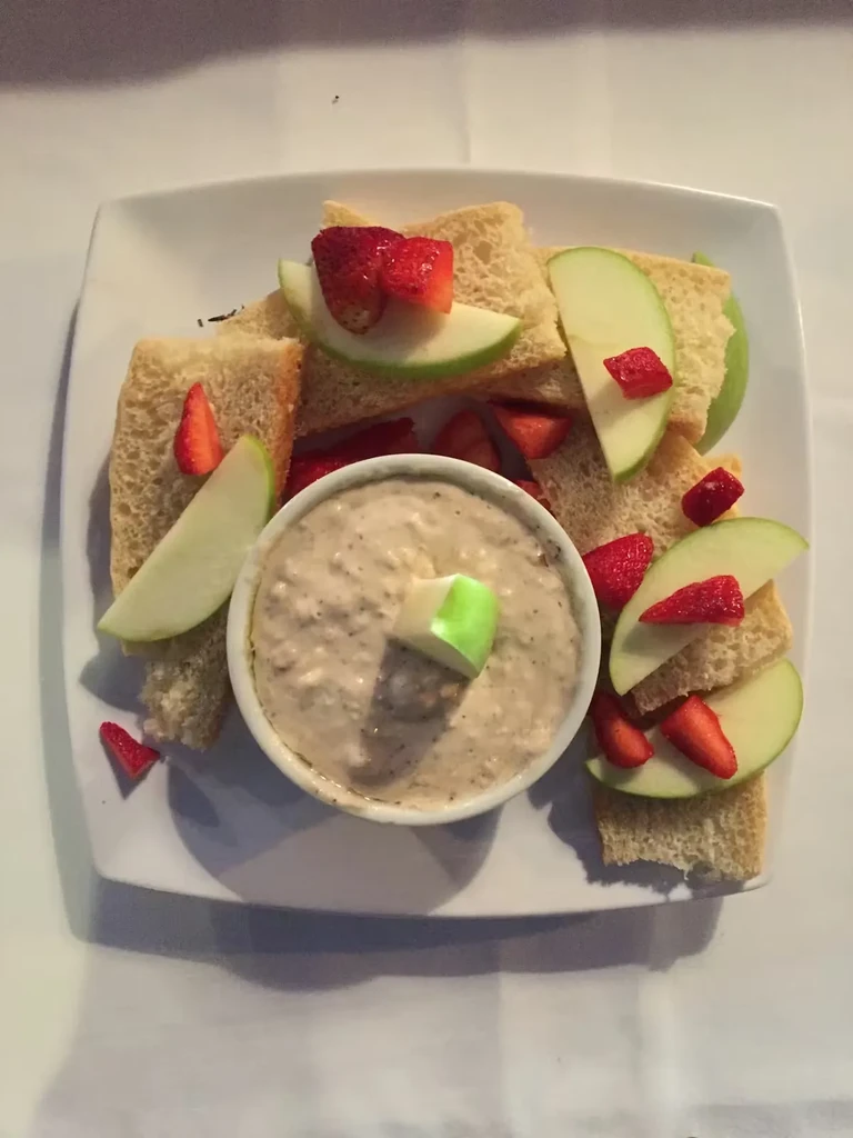 Beige dip surrounded by green apple, red strawberries, and bread.