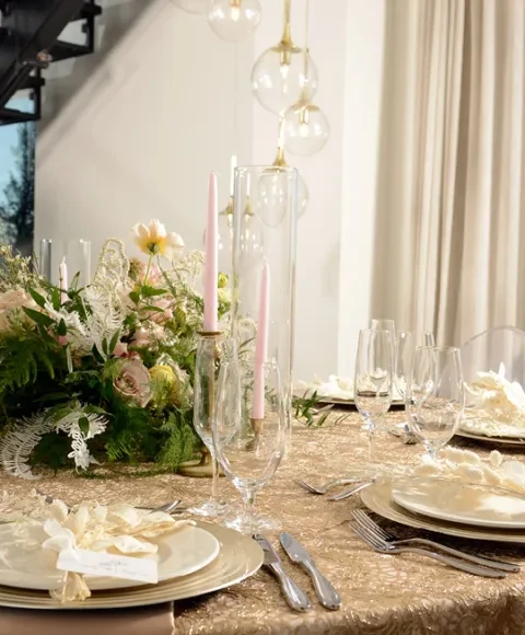 Gold sequined dining table with floral centerpiece, pink candles, and place settings.