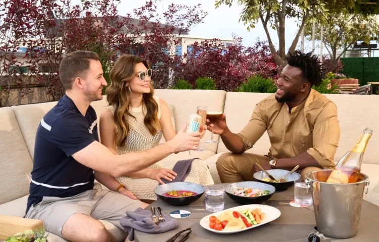 Three people toast with food and drinks on an outdoor patio.