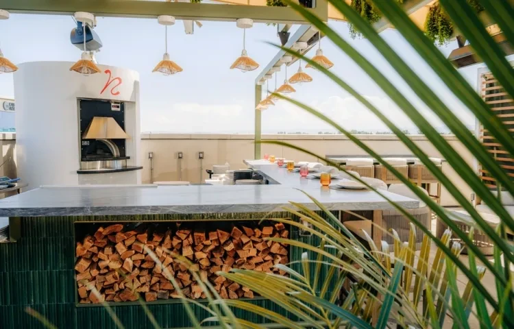 Rooftop bar with modern white pizza oven, firewood, and foliage.