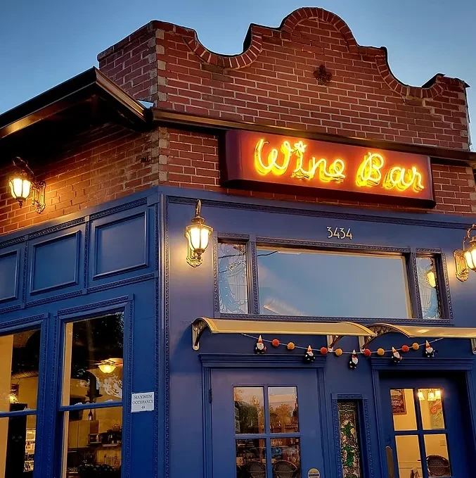 Dusk view of 'Wine Bar' building, brick and blue, with glowing sign.