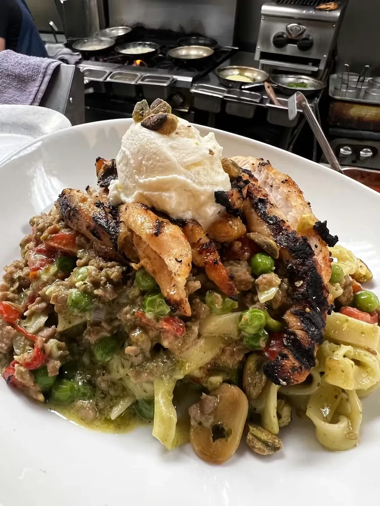 Grilled chicken, green pasta with meat, topped with creamy cheese and pistachios.