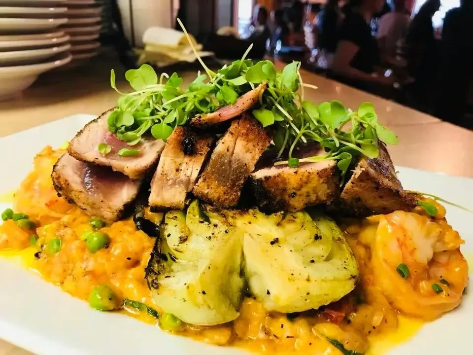 Restaurant dish of seared tuna, shrimp, and vegetables on orange sauce.