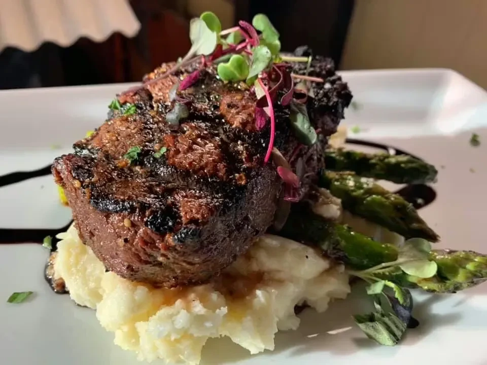 Plated grilled steak, mashed potatoes, asparagus, microgreens, and sauce.