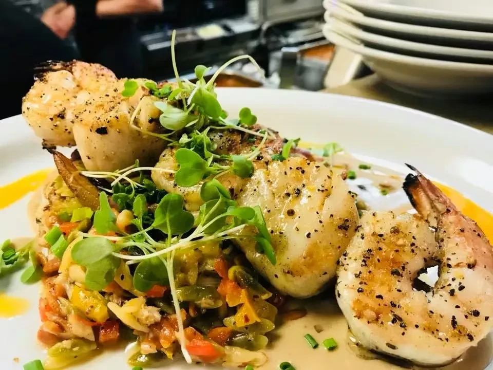 Plated pan-seared scallops and shrimp with vegetables, microgreens, and sauce.
