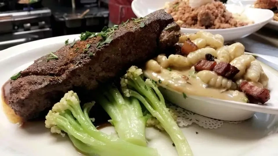 Plated seared meat, broccoli, and creamy gnocchi with crispy bacon.