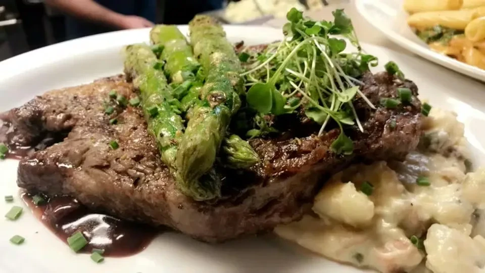 Grilled meat, asparagus, creamy side, dark sauce on white oval plate.