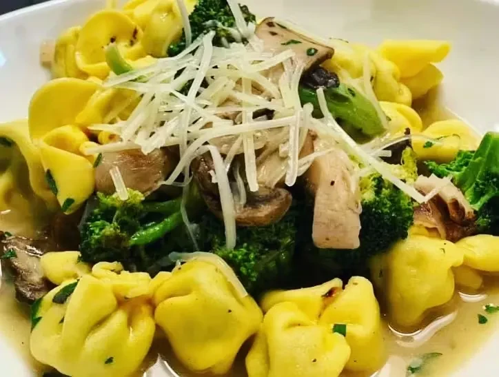 Yellow tortellini pasta with broccoli, mushrooms, sauce, and grated cheese.