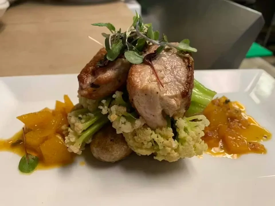 Seared meat, green cauliflower, roasted vegetables, and orange sauce.