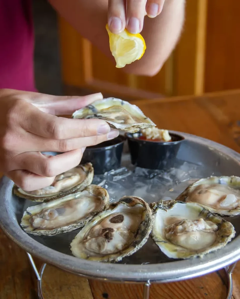 Hands squeezing lemon over fresh oysters on ice with sauces.