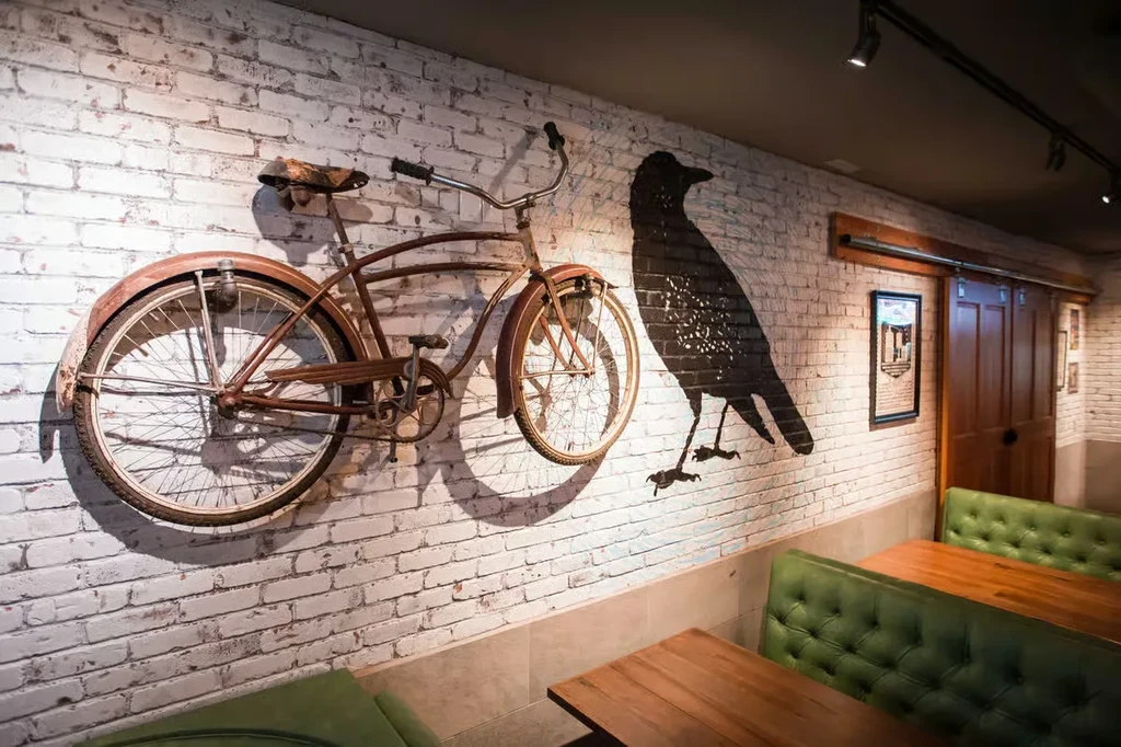 Restaurant interior: brick wall with antique bicycle, crow art, and green booths.