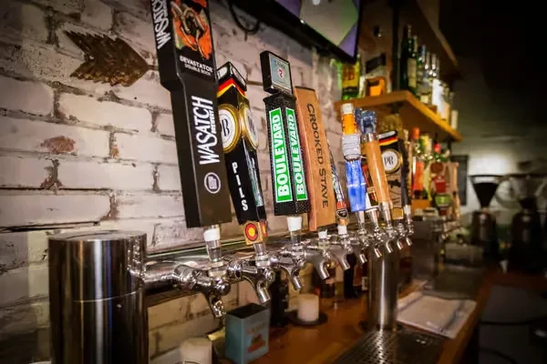 Row of ten distinct beer taps with brewery logos at a bar.