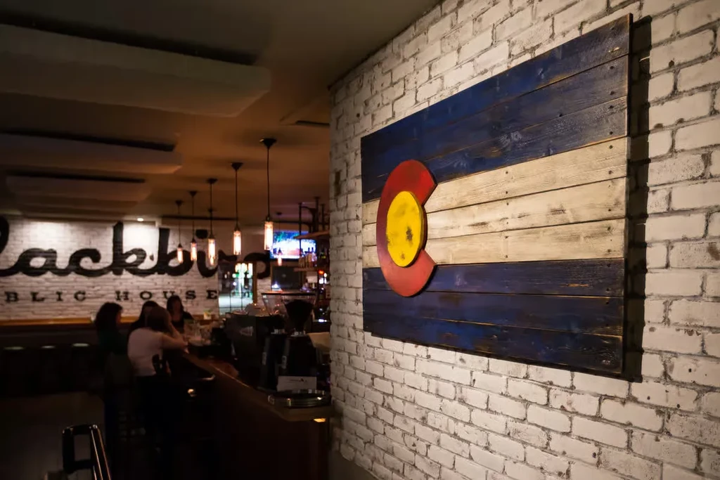 Rustic wooden Colorado flag art on a pub's white brick wall.
