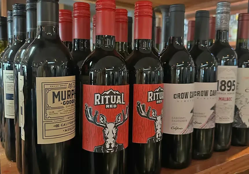 Red wine bottles, including 'Ritual Red' and 'Murphy-Goode', on a wooden shelf.