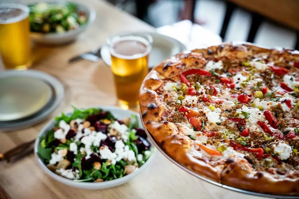 Close-up of a meat pizza, green salad, and two beers on table.