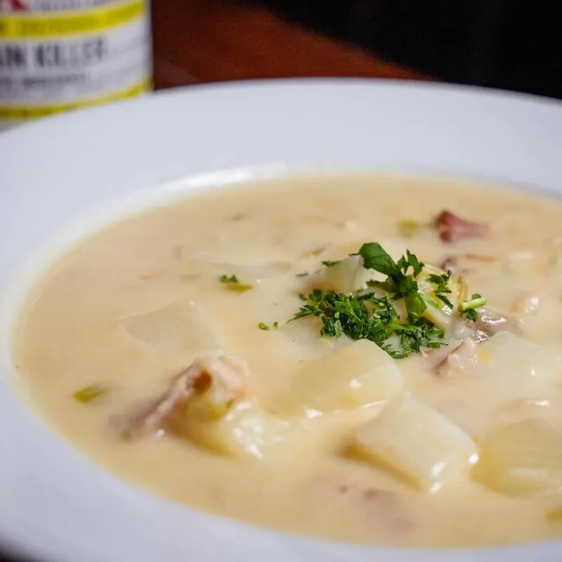 White bowl of creamy chowder with potatoes, meat, and parsley garnish.