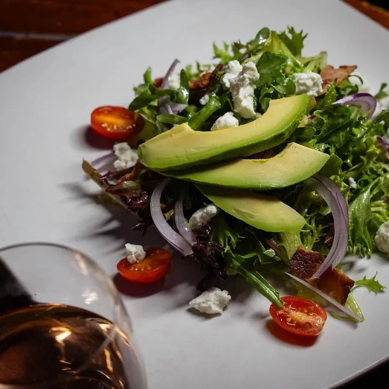 Colorful salad with greens, avocado, cheese, tomatoes, and bacon.