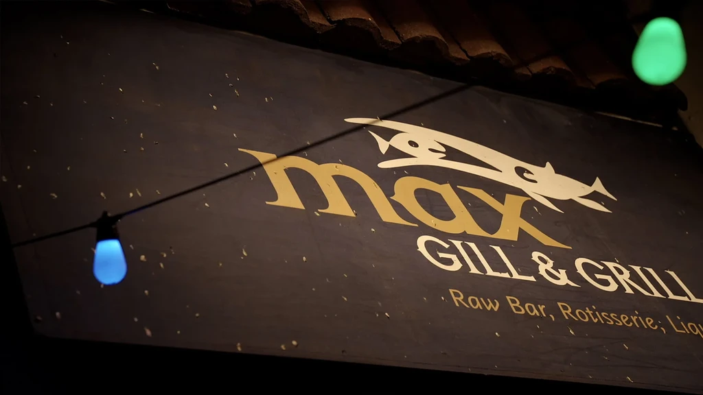 Dark "max GILL & GRILL" sign, white fish, glowing string lights.