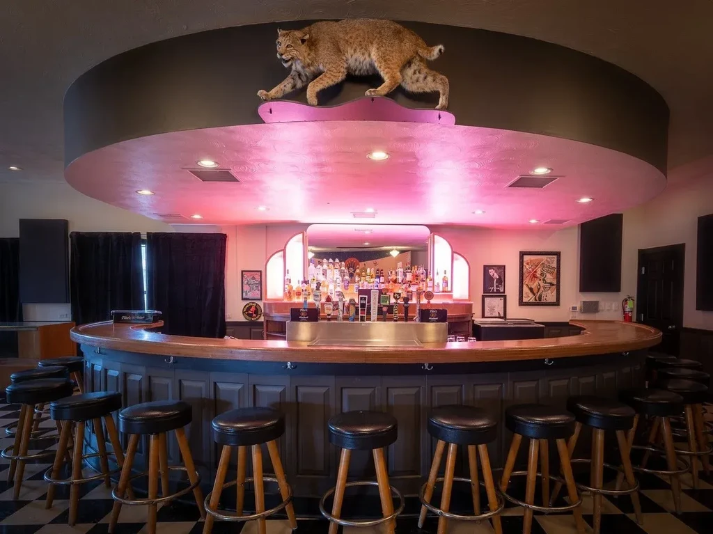 Empty bar with pink-lit ceiling, dark wood counter, and a bobcat.