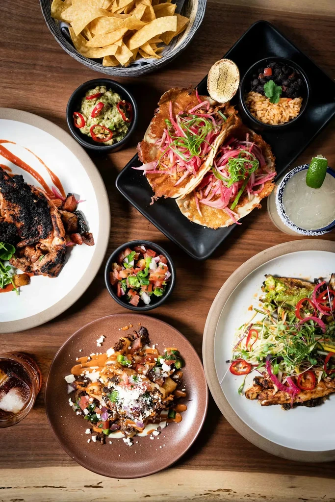 Overhead shot of colorful Mexican food and drinks on a wooden table.