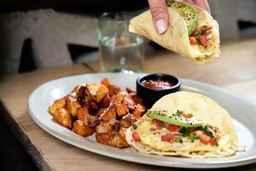 Hand holding breakfast taco with eggs, pico, avocado, and roasted potatoes.