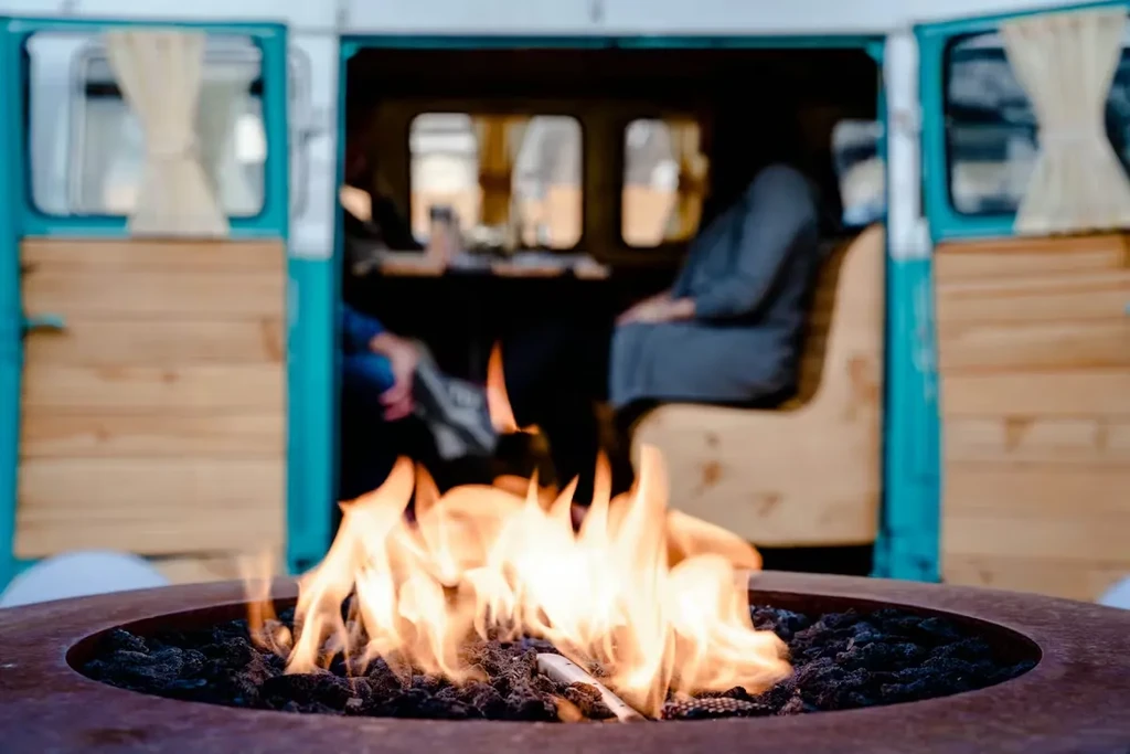 Bright flames in rustic fire pit, blurred vintage turquoise van with figures.