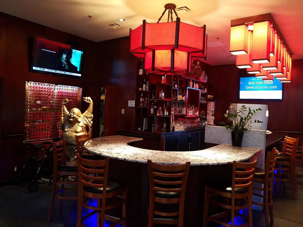 Asian-inspired restaurant bar with red lanterns and a laughing Buddha statue.