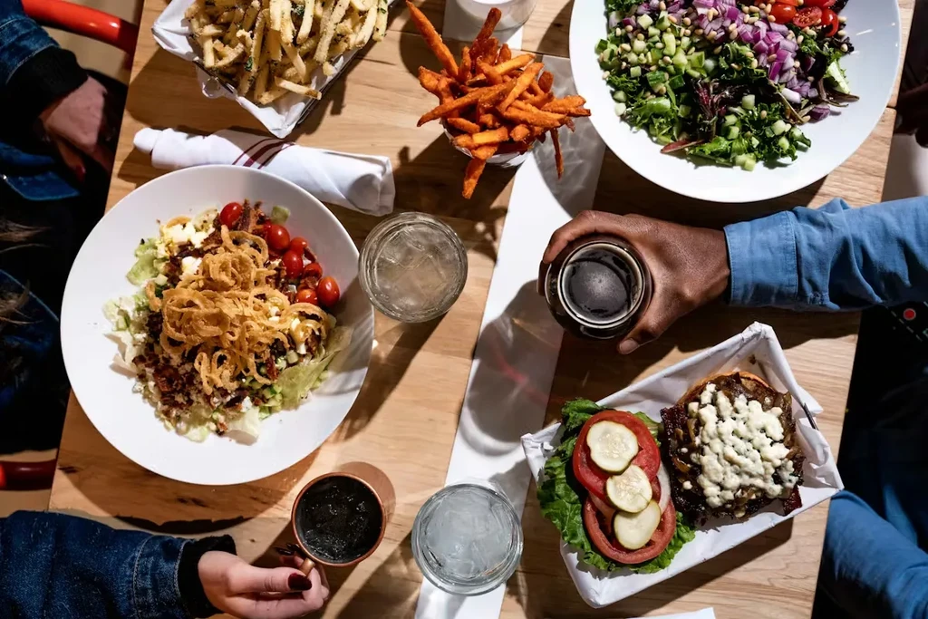 Overhead of restaurant table with salads, fries, burger, and drinks.