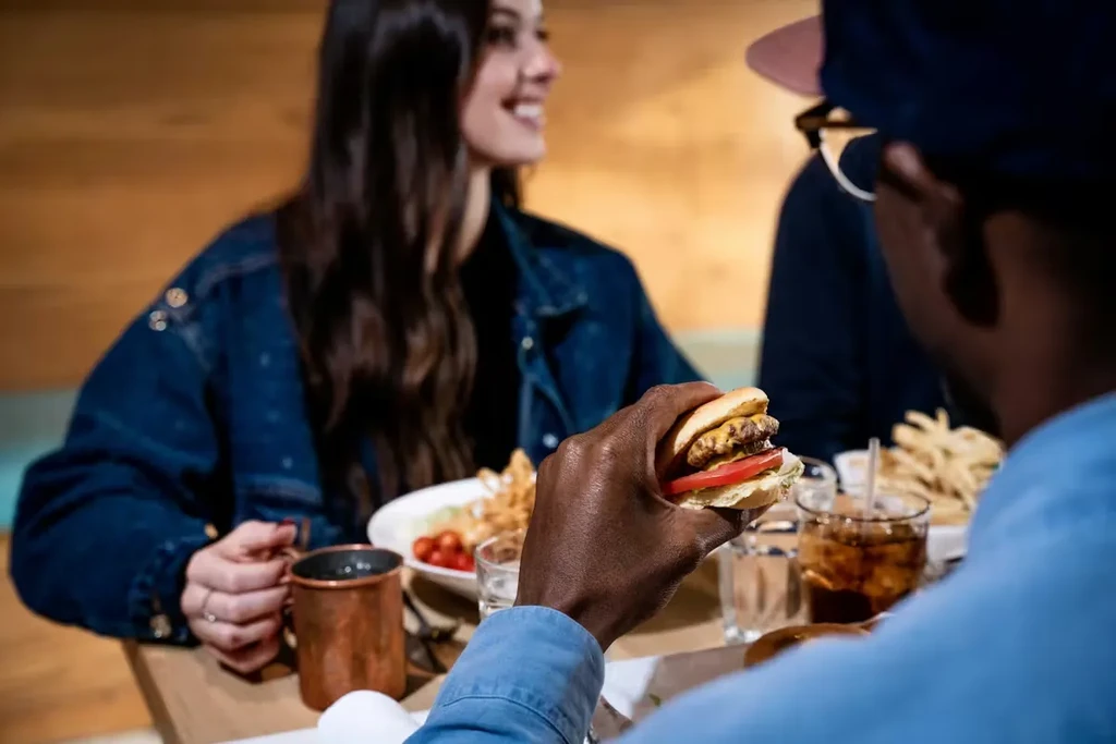 Person holds double-patty cheeseburger, fries and drinks in restaurant.