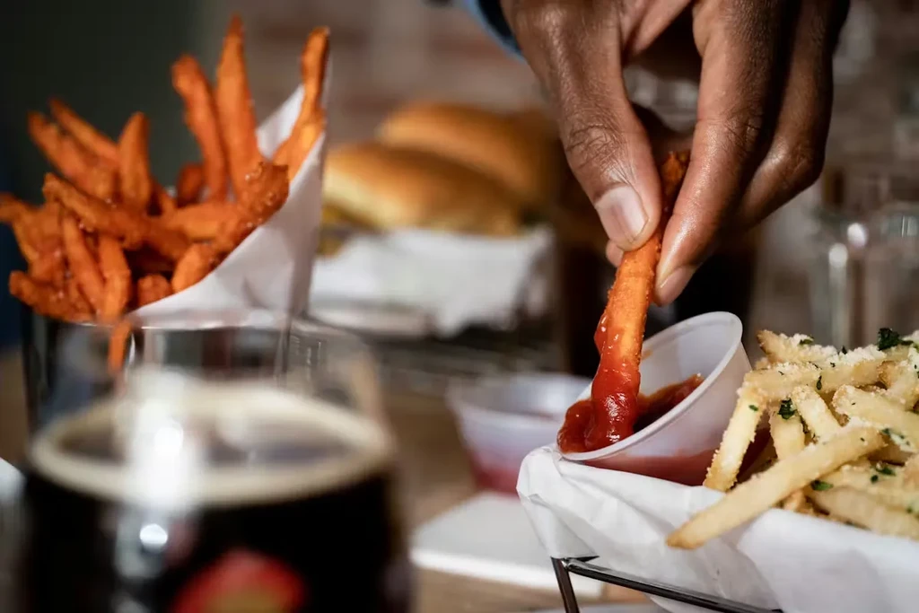 Dark-skinned hand dips ketchup-covered sweet potato fry into more.