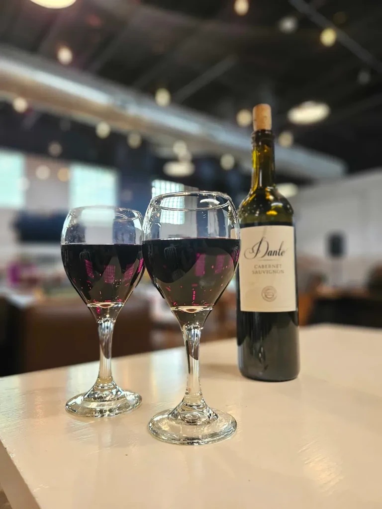 Two glasses of red wine beside an uncorked Dante Cabernet Sauvignon bottle.
