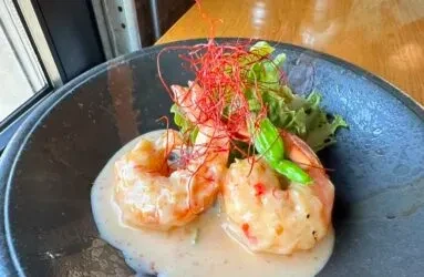 Two shrimp in creamy sauce, garnished with lettuce, basil, red spices.