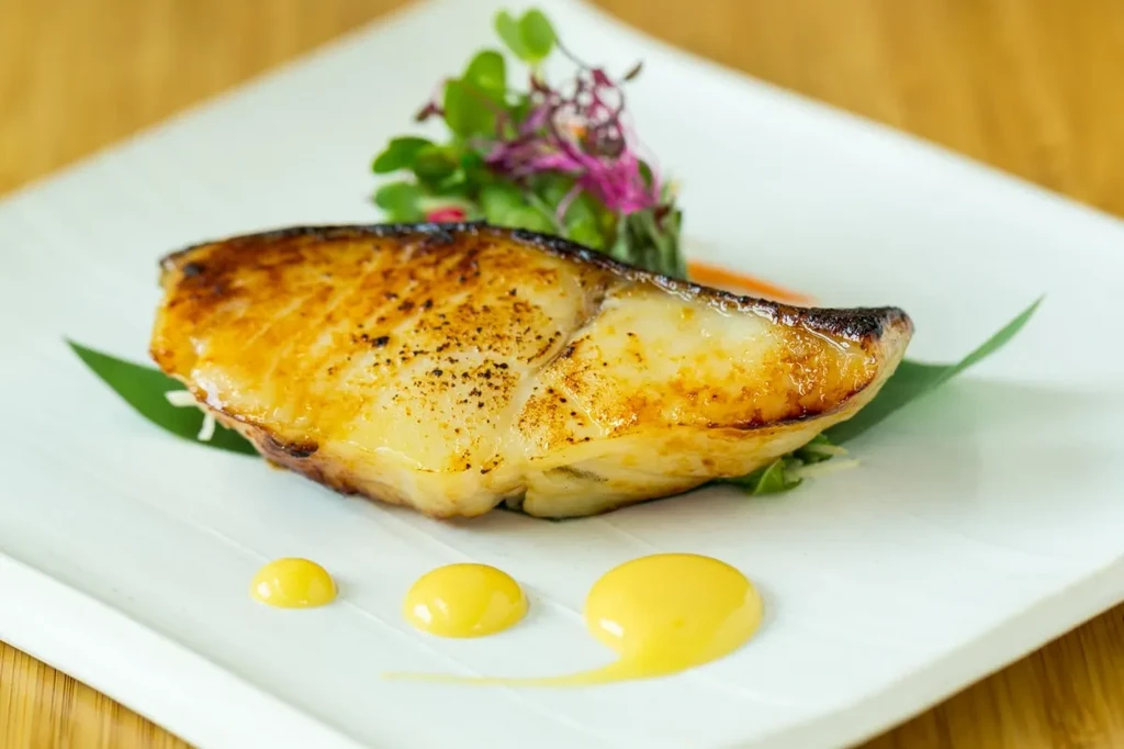 Plated grilled fish with microgreens, purple garnish, and yellow sauce.
